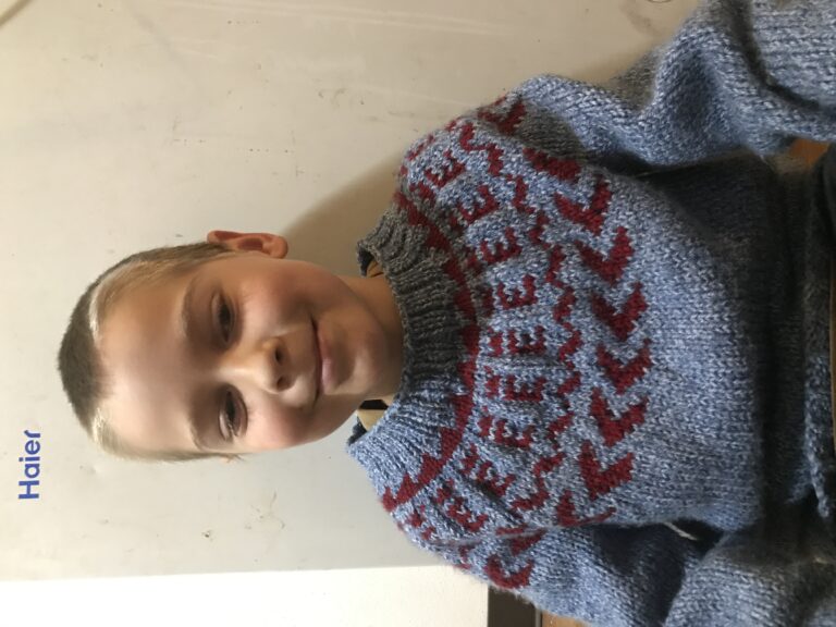 my 9-year-old son, sitting on the floor. he is wearing a blue and red hand knit sweater.