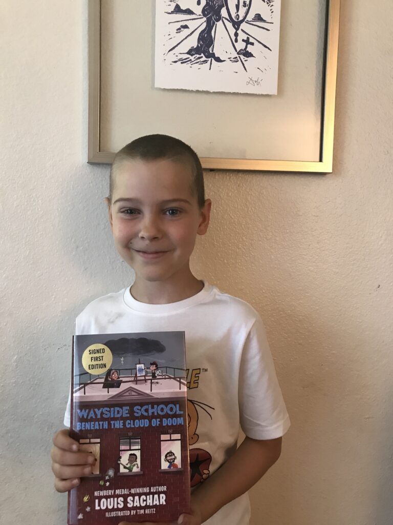 my 9-year-old son standing up and holding his copy of the book "wayside school beneath the cloud of doom"